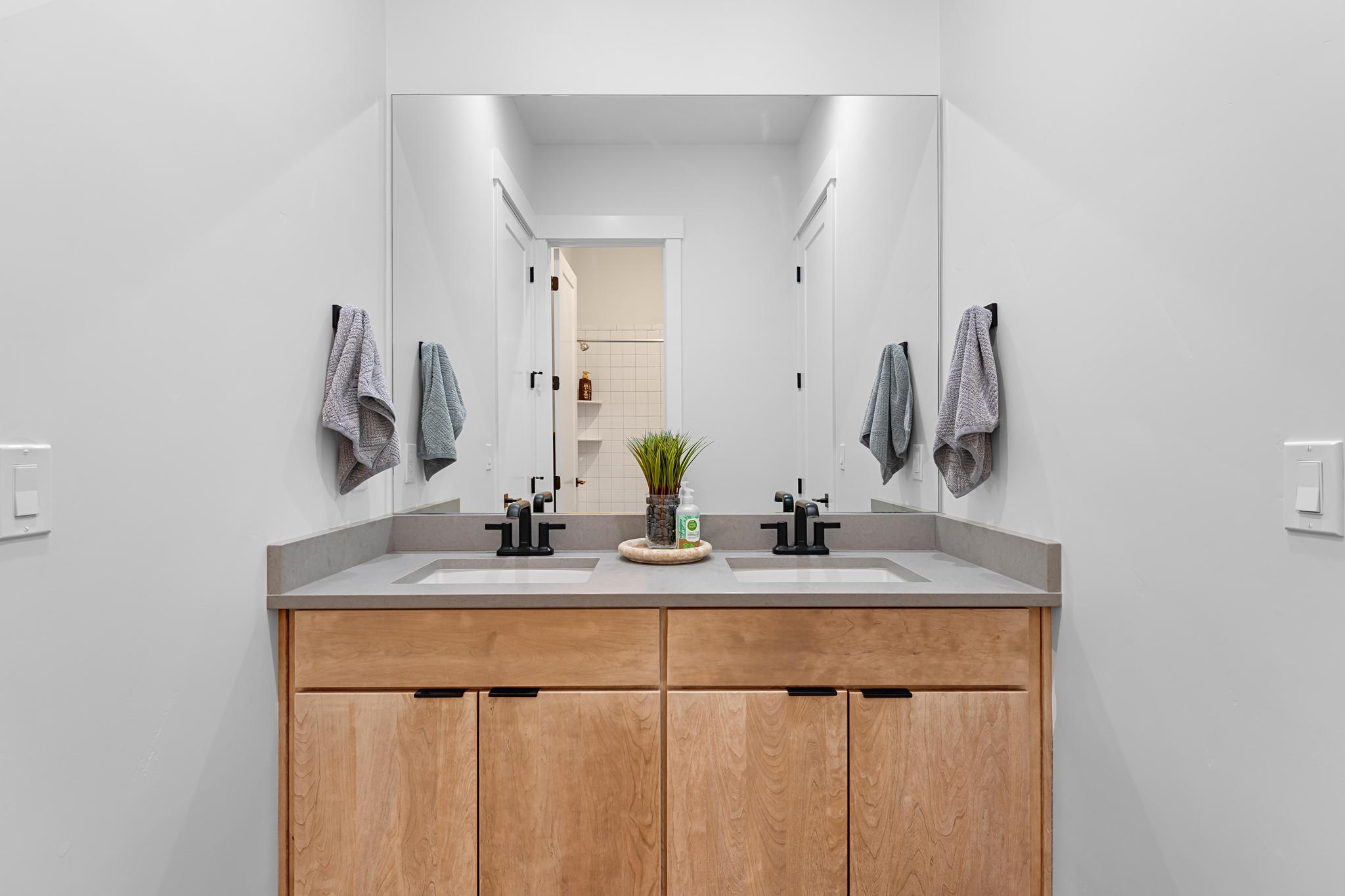 Double vanity with light wood-finish cabinetry, integrated sinks, black hardware, and an expansive mirror