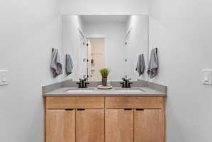 Double vanity with light wood-finish cabinetry, integrated sinks, black hardware, and an expansive mirror