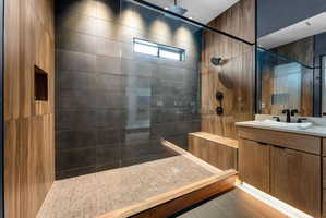 Spacious shower enclosure with wood-finish paneling, dark large-format tile, glass partition, and integrated bench seating