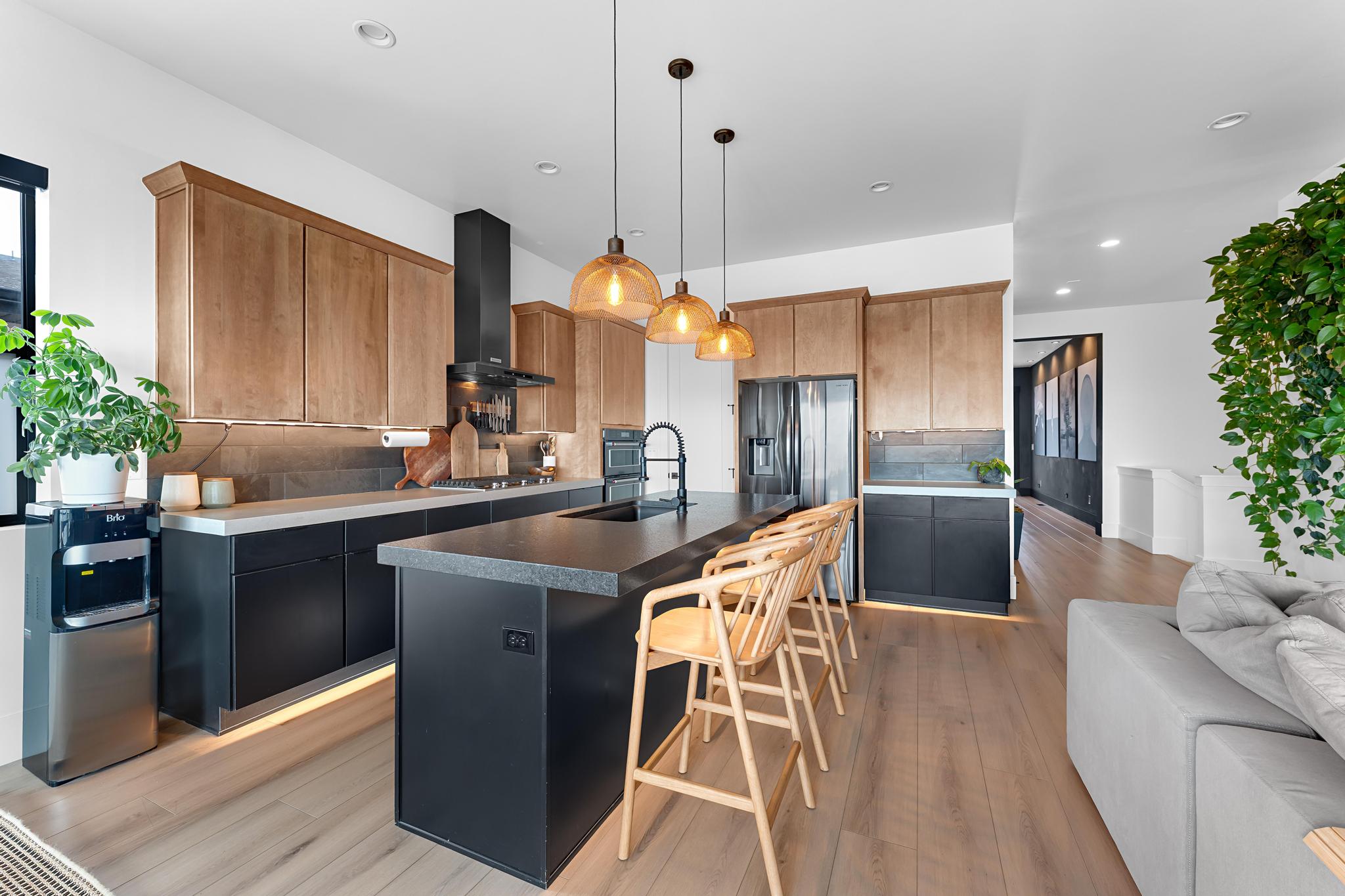 Modern kitchen featuring light wood-finish upper cabinetry, black lower cabinetry, and a substantial center island with seating for four