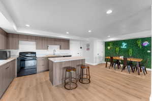 Modern kitchen with light wood-finish cabinetry, solid surface countertops, and a full suite of black appliances