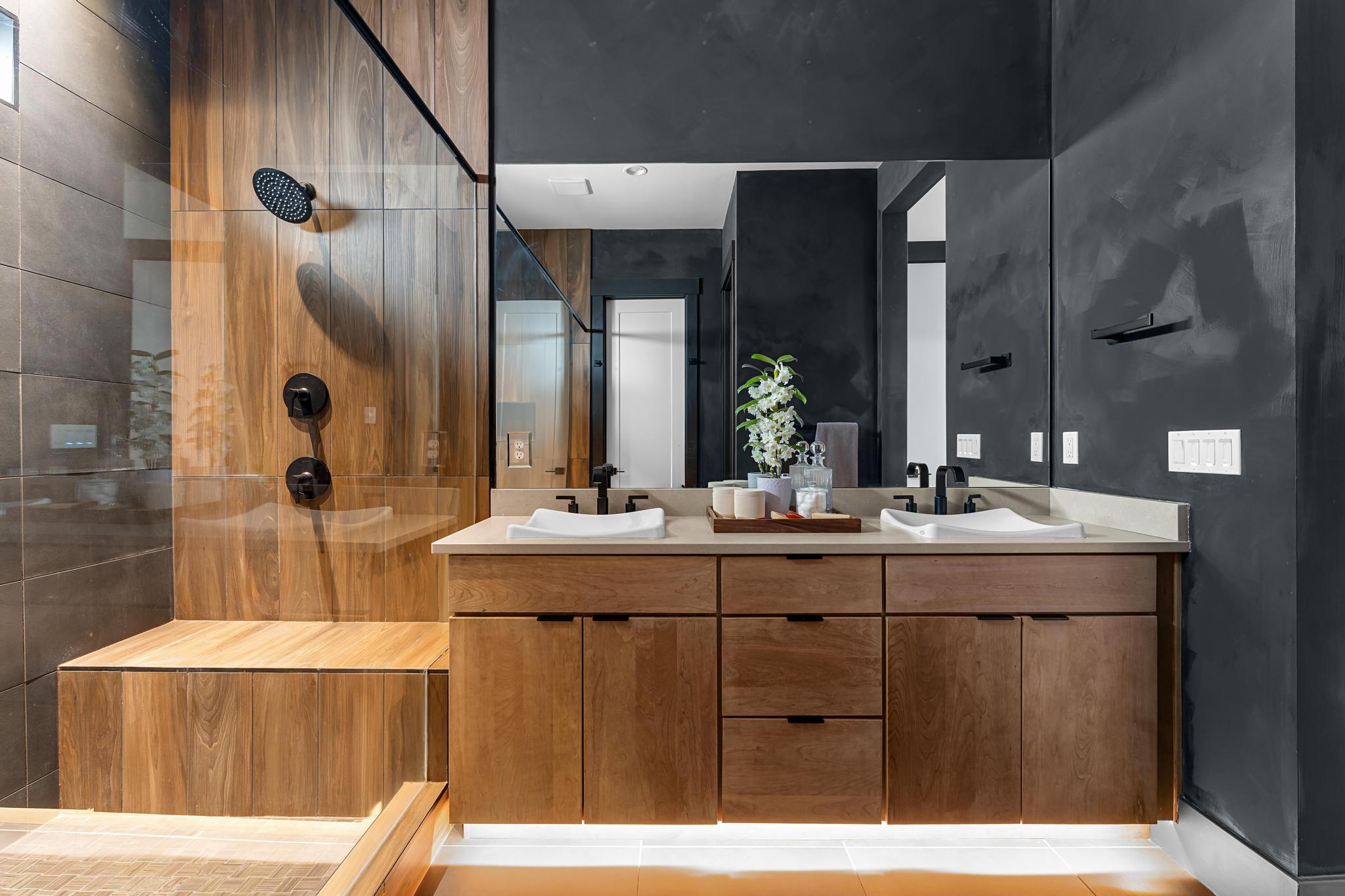 Modern bathroom featuring a dual vanity with light wood-finish cabinetry, white vessel sinks, and matte black fixtures