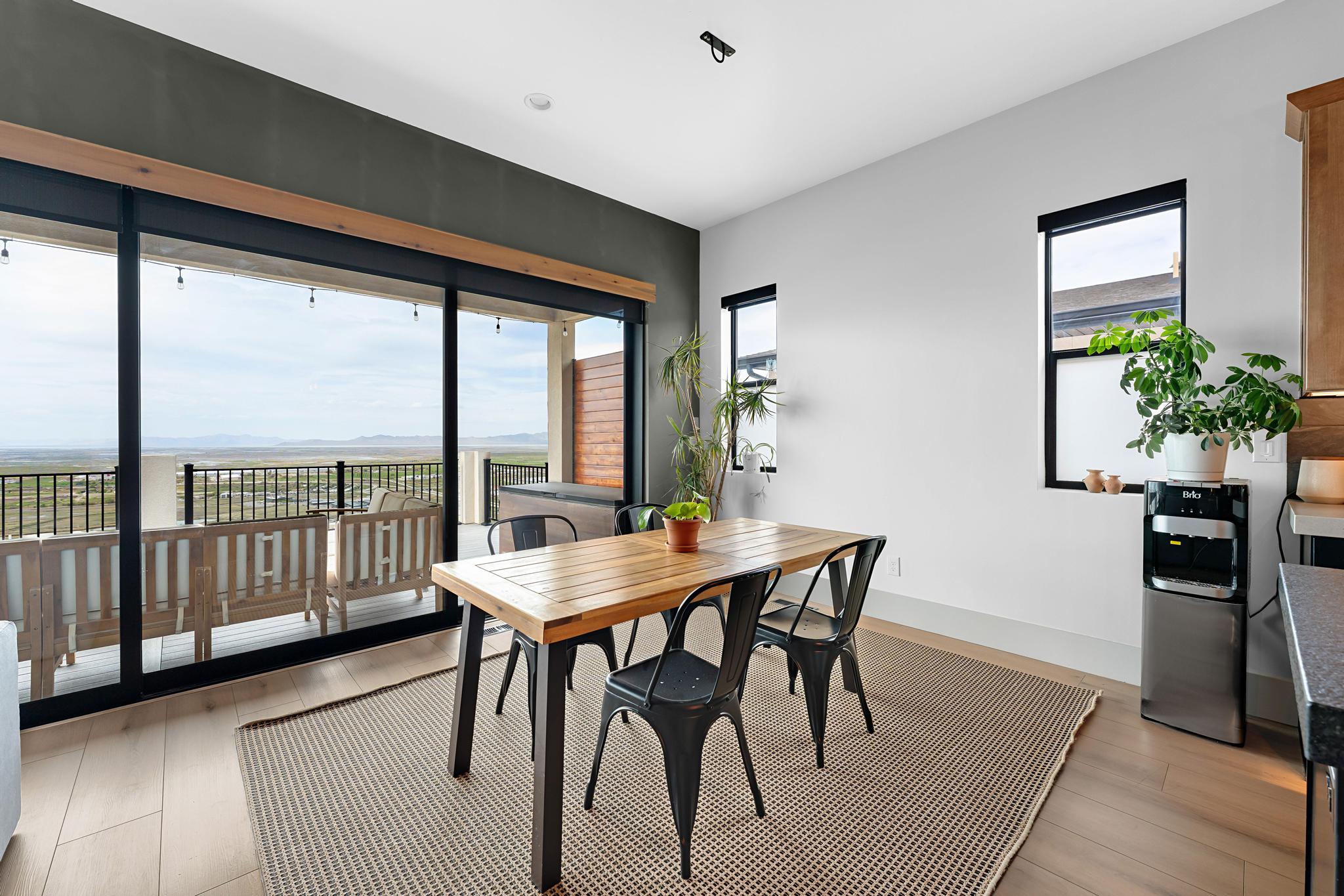 Open-concept dining area featuring light wood-finish flooring, a contemporary ceiling light fixture, and a large sliding glass door opening to an outdoor patio with black metal railings