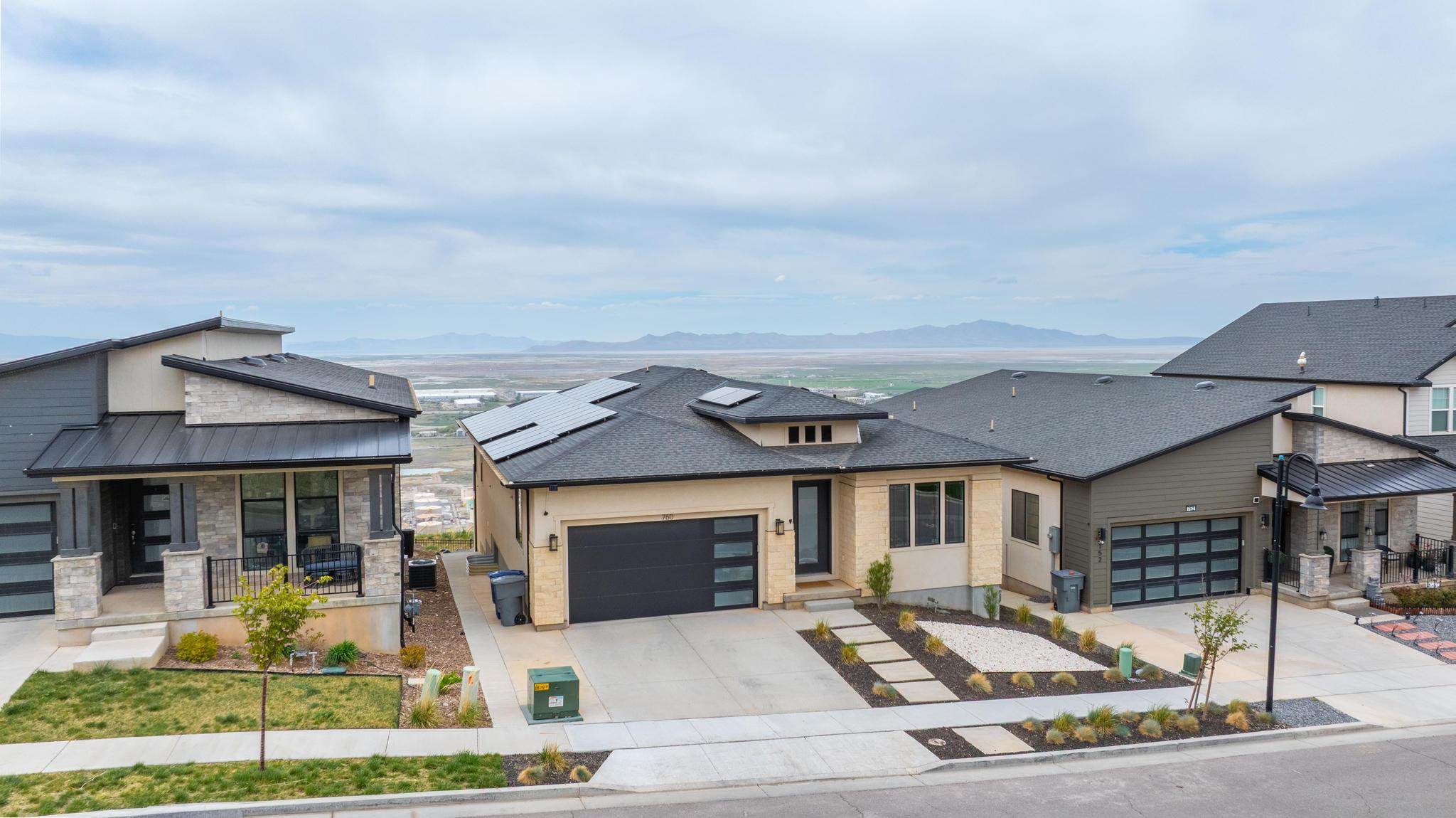 Contemporary home exterior featuring a light-toned facade with stone accents, a dark-toned garage door, and solar panels on the roof
