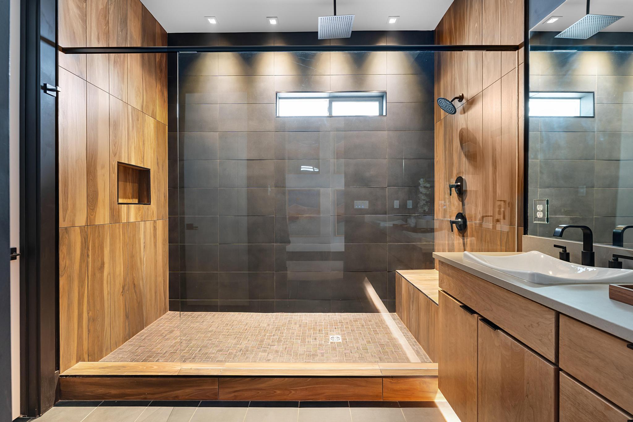 Spacious shower enclosure with glass paneling, dark tile walls, wood-finish paneling, and a built-in shower niche