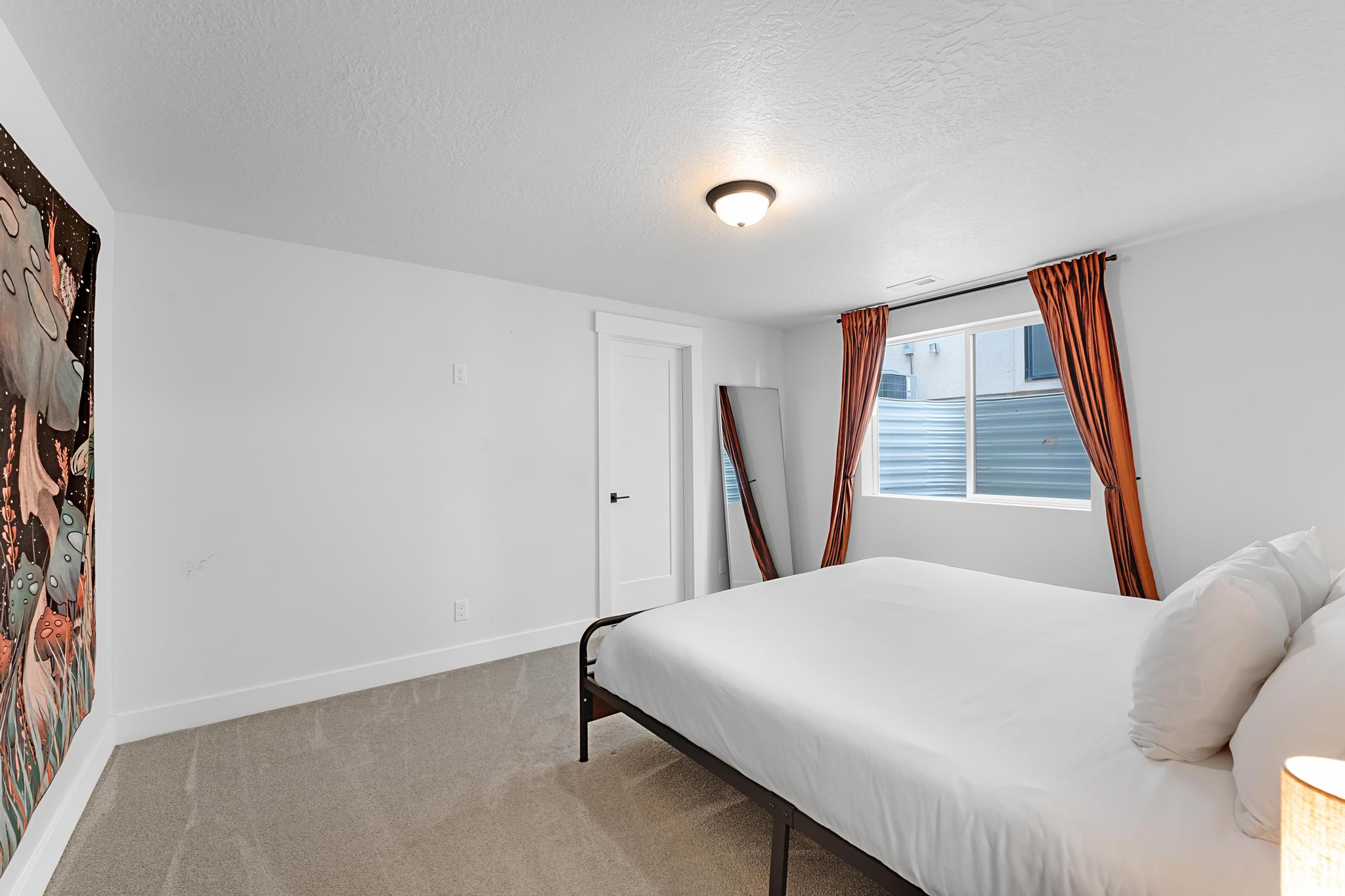 Carpeted room featuring a single window, a flush-mount ceiling light, a solid white door with black hardware, and white baseboards
