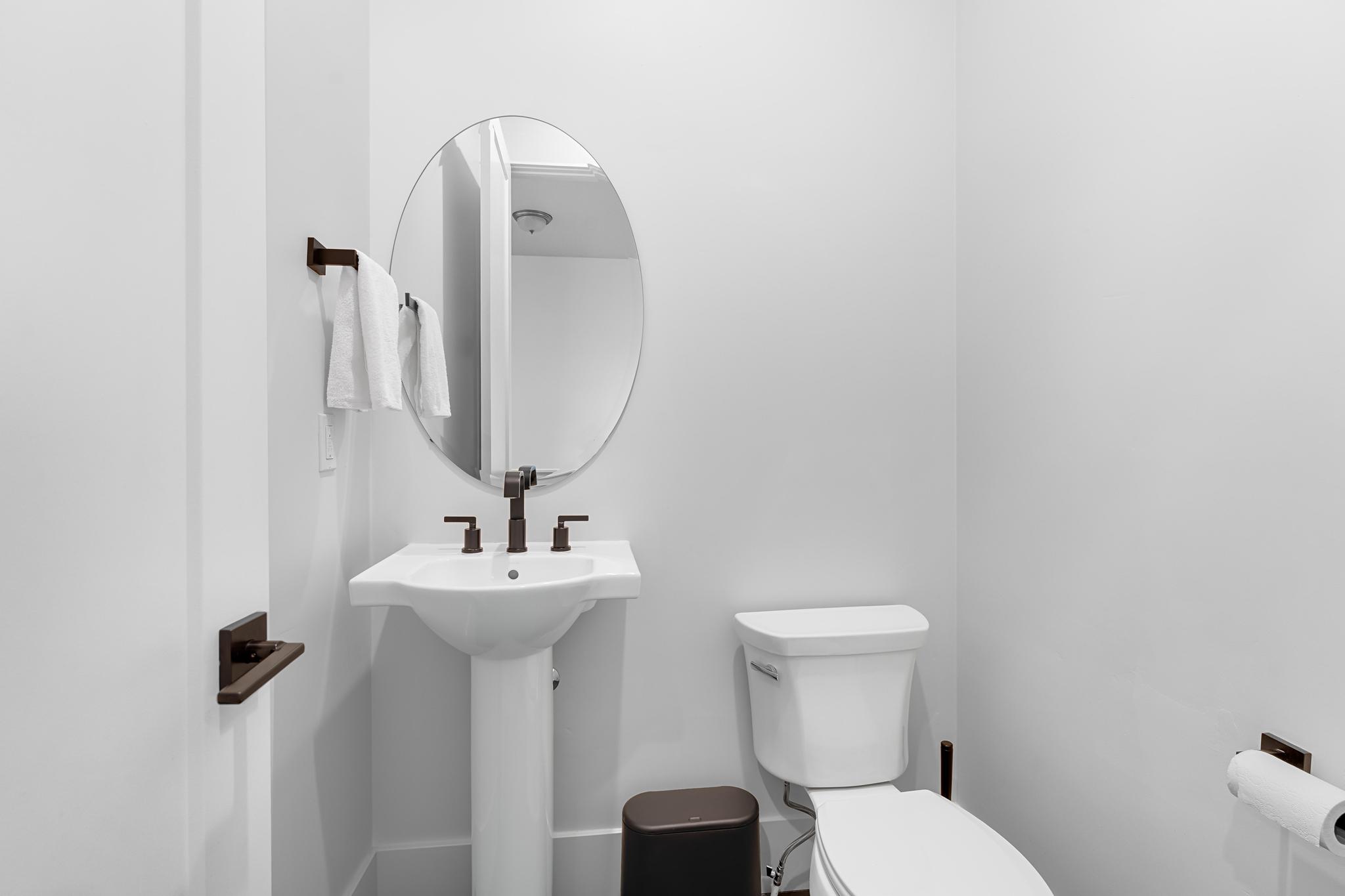 Pedestal sink with dark bronze hardware, oval mirror, and white toilet