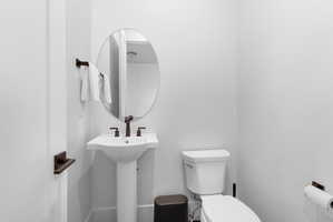 Pedestal sink with dark bronze hardware, oval mirror, and white toilet