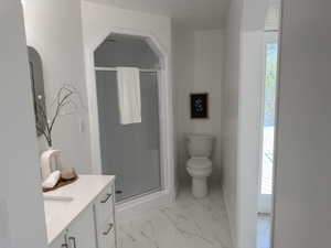 Bathroom featuring a glass-enclosed shower, white vanity with integrated sink, white cabinetry with silver hardware, and a toilet