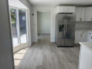 Kitchen featuring wood-finish flooring, white cabinetry, a stainless steel refrigerator, and light-toned countertops