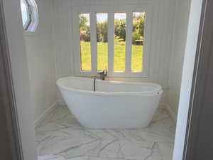 Freestanding soaking tub with a floor-mounted faucet, set against white shiplap walls and large format marble-look tile flooring