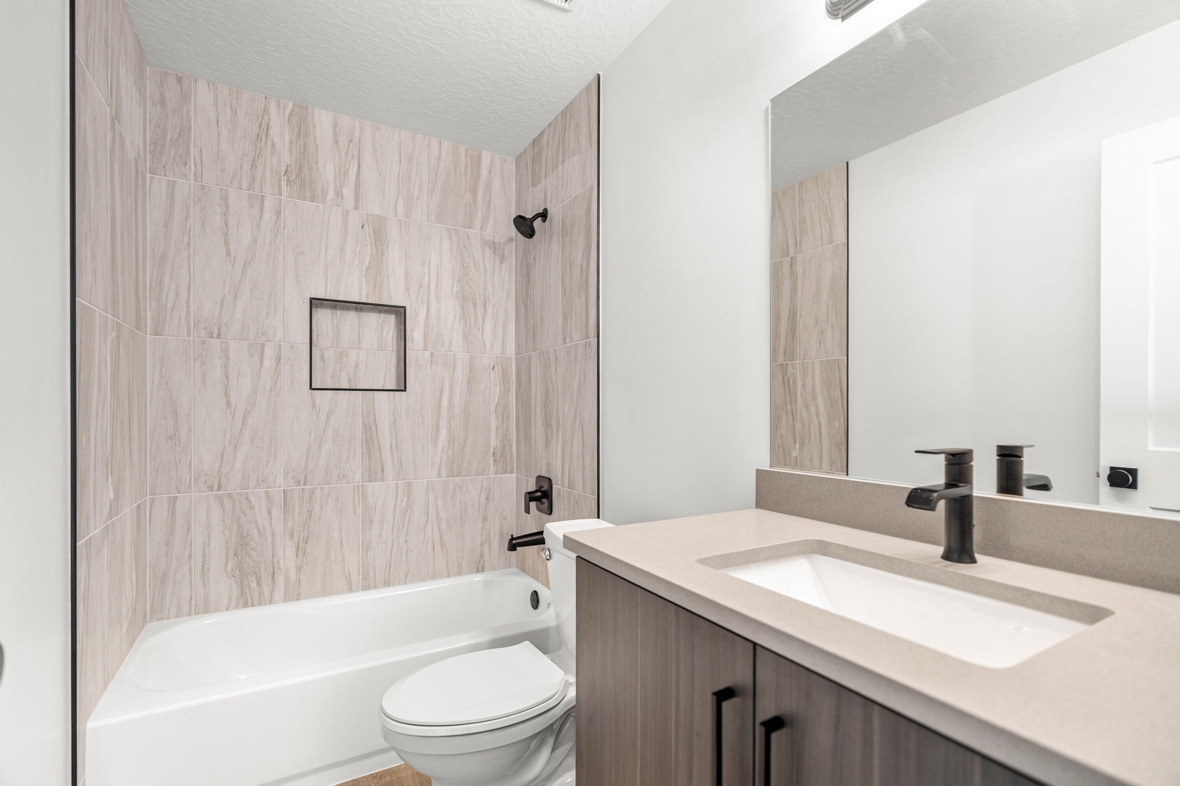 Bathroom featuring a built-in tub with a tiled surround, integrated shower niche, and matte black fixtures