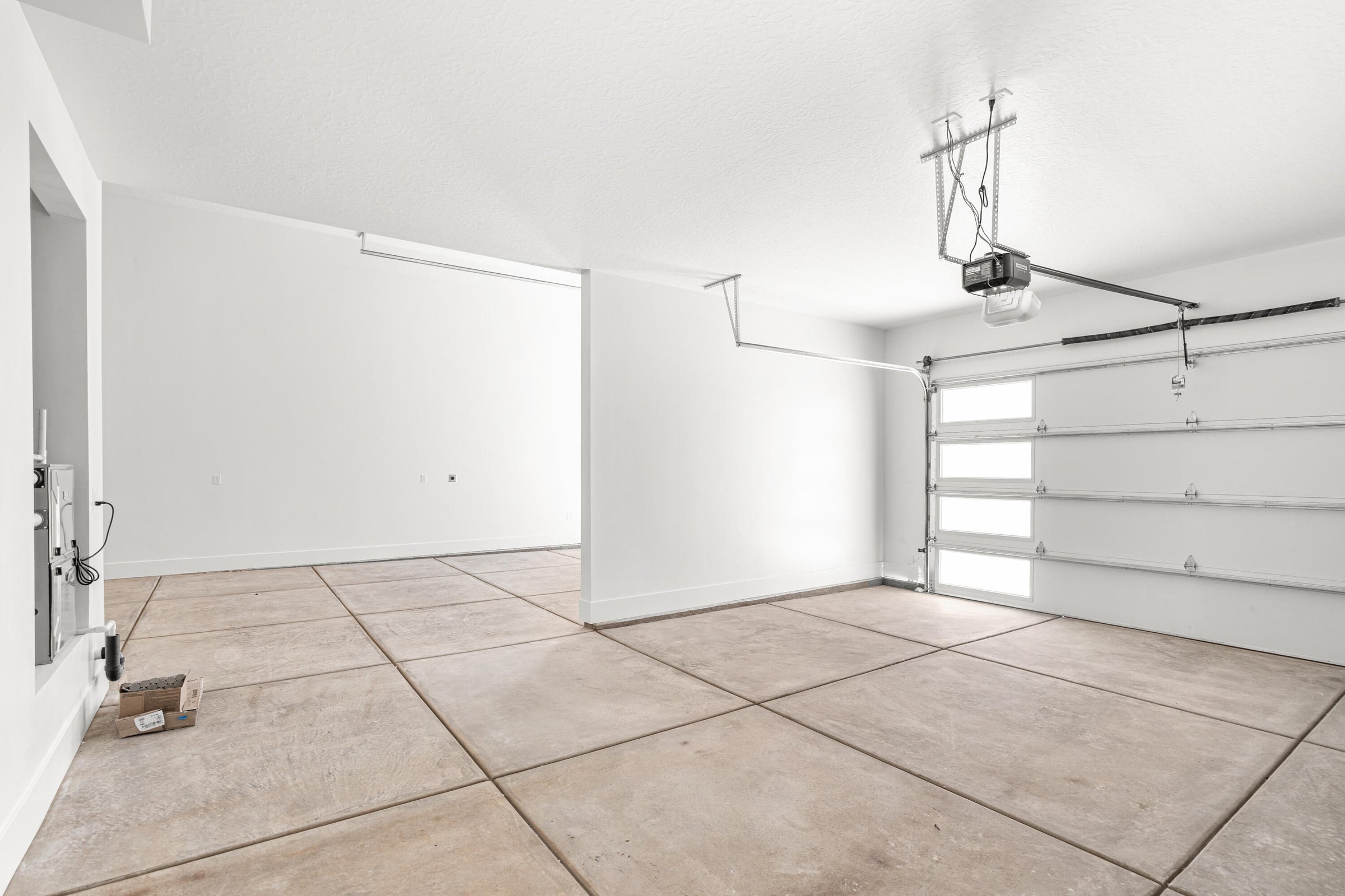 Spacious garage with light-colored concrete flooring, white walls, and an automatic garage door opener