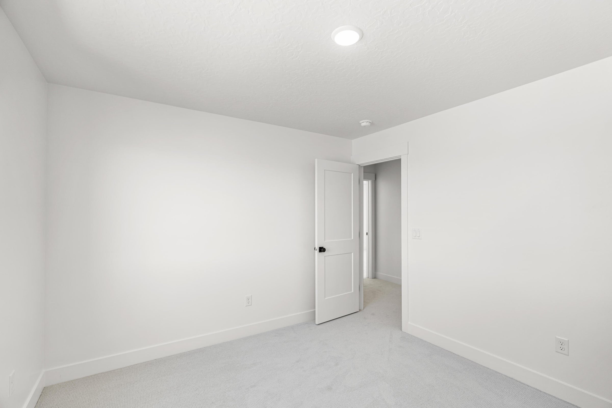 Neutral-toned room featuring a single recessed light, white walls, and light-colored carpeting