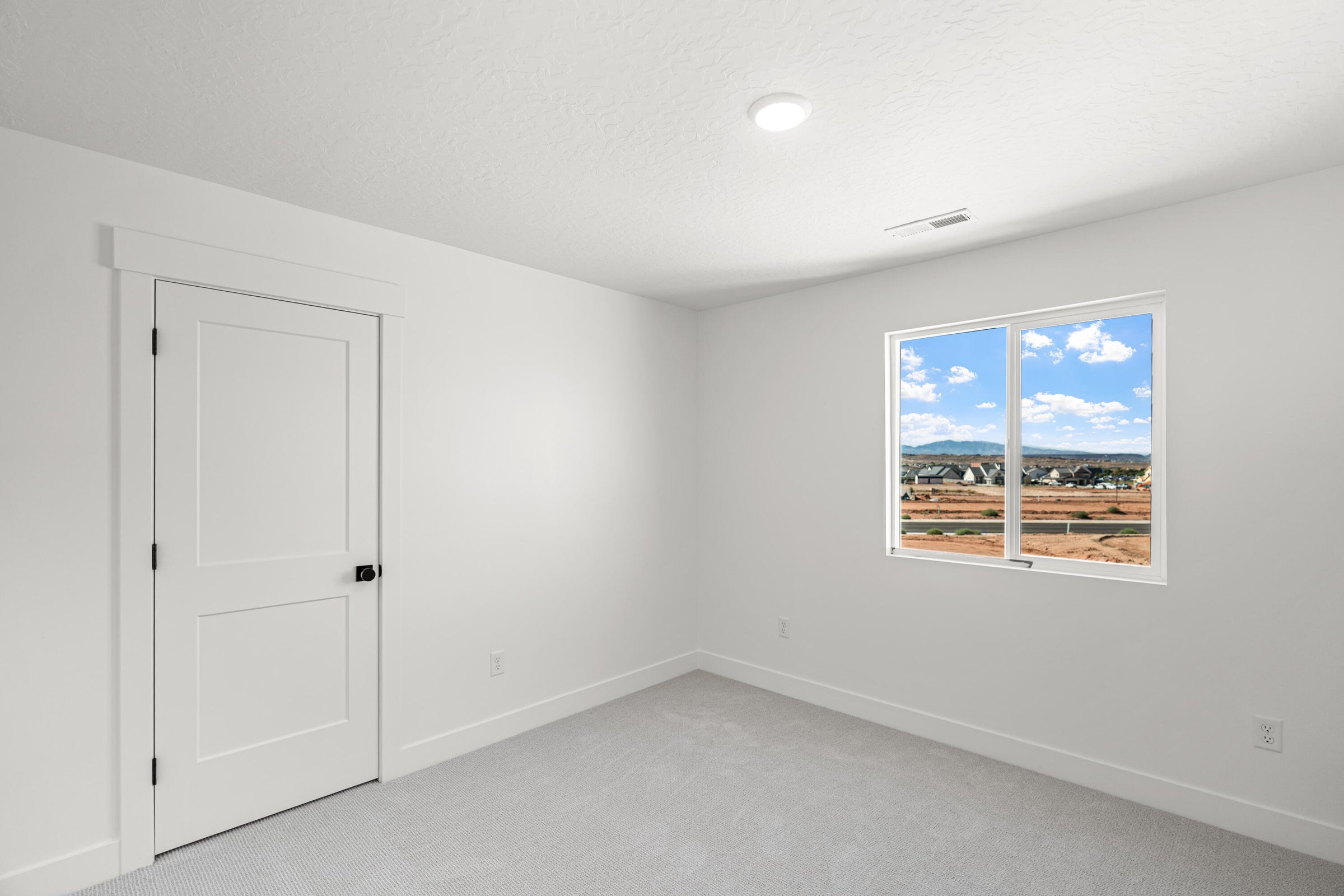 White interior room featuring light-colored carpeting, a contemporary two-panel door with matte black hardware, and a window offering expansive landscape views