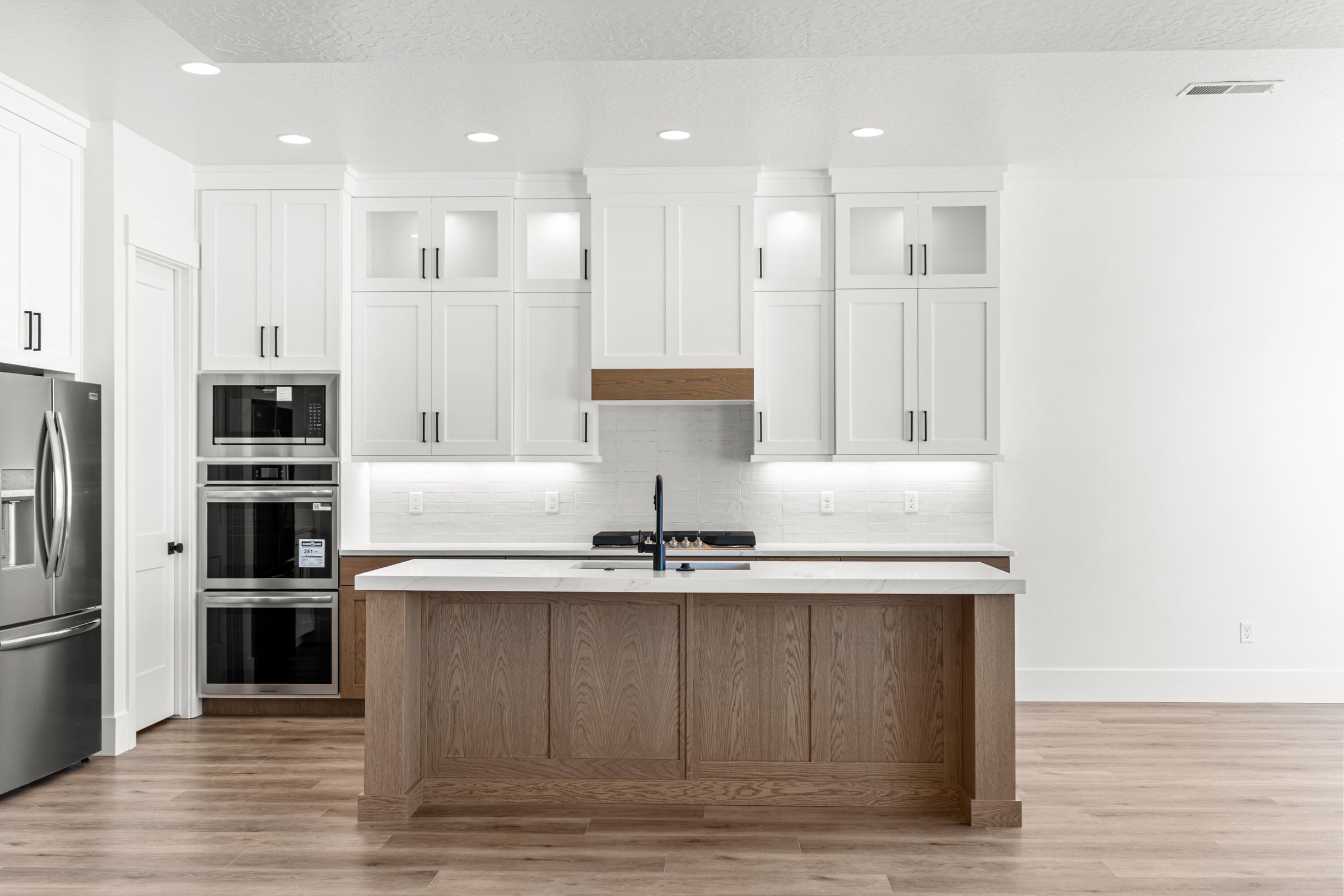Gourmet kitchen featuring a wood-finish island with a sink, white shaker cabinetry, stainless steel appliances, and wood-finish flooring