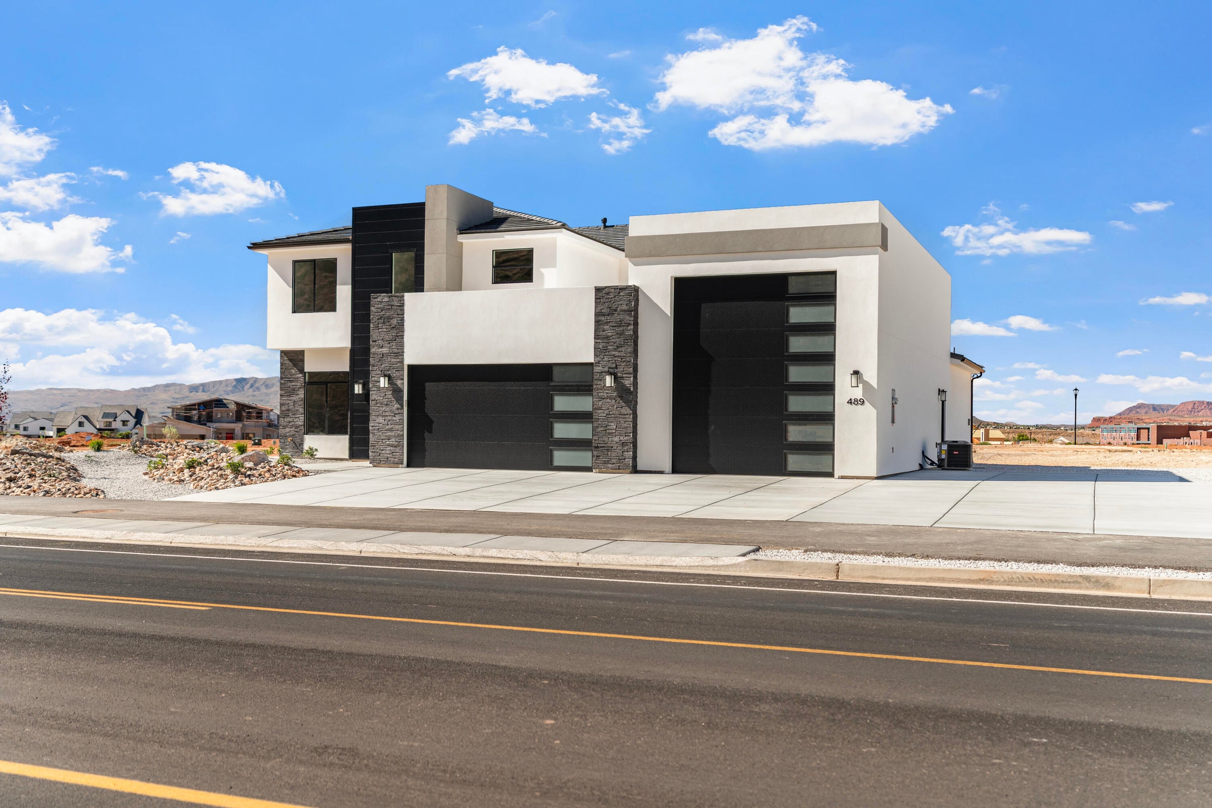 Contemporary architectural design featuring a white stucco exterior, dark stone accents, and multiple black garage doors with frosted glass panels