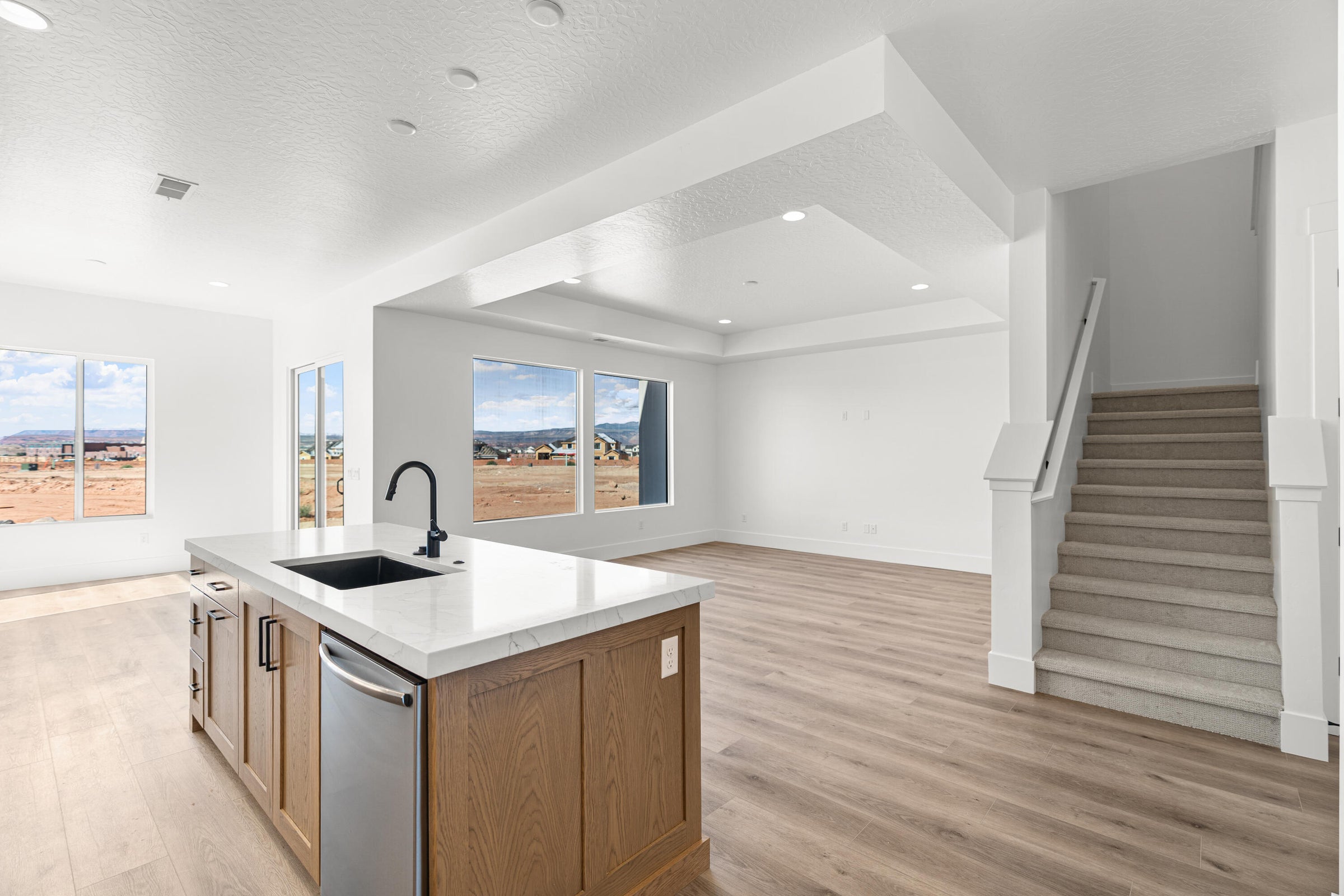 Kitchen island with wood-finish cabinetry, light-toned countertop, and undermount sink with black faucet