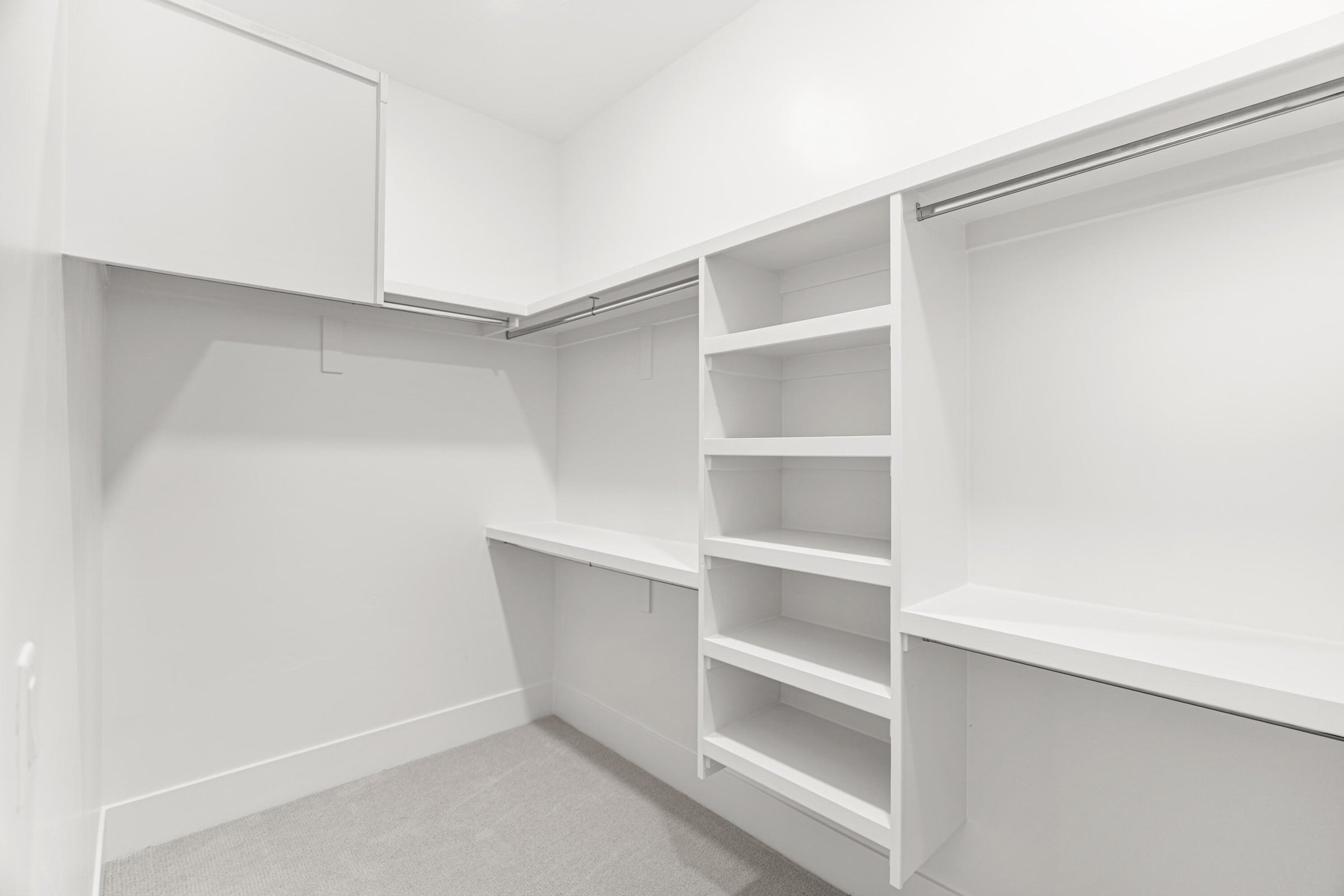 Spacious walk-in closet featuring built-in shelving, hanging rods, upper cabinetry, and carpet flooring