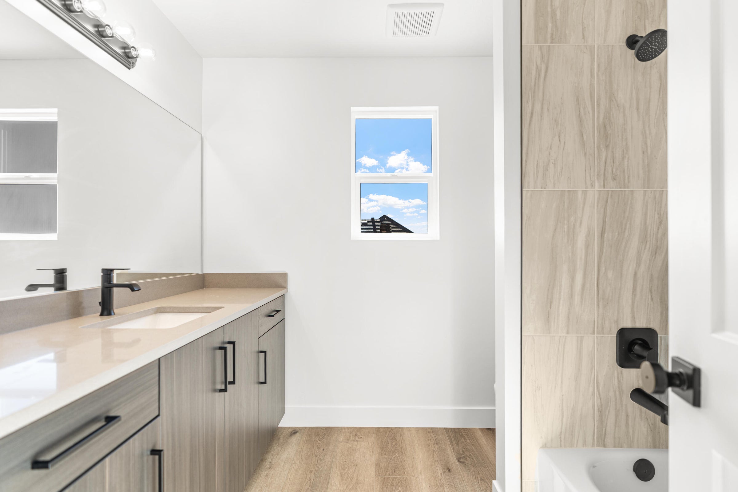 Bathroom featuring a vanity with an integrated sink, light-toned countertop, and wood-finish cabinetry with matte black hardware