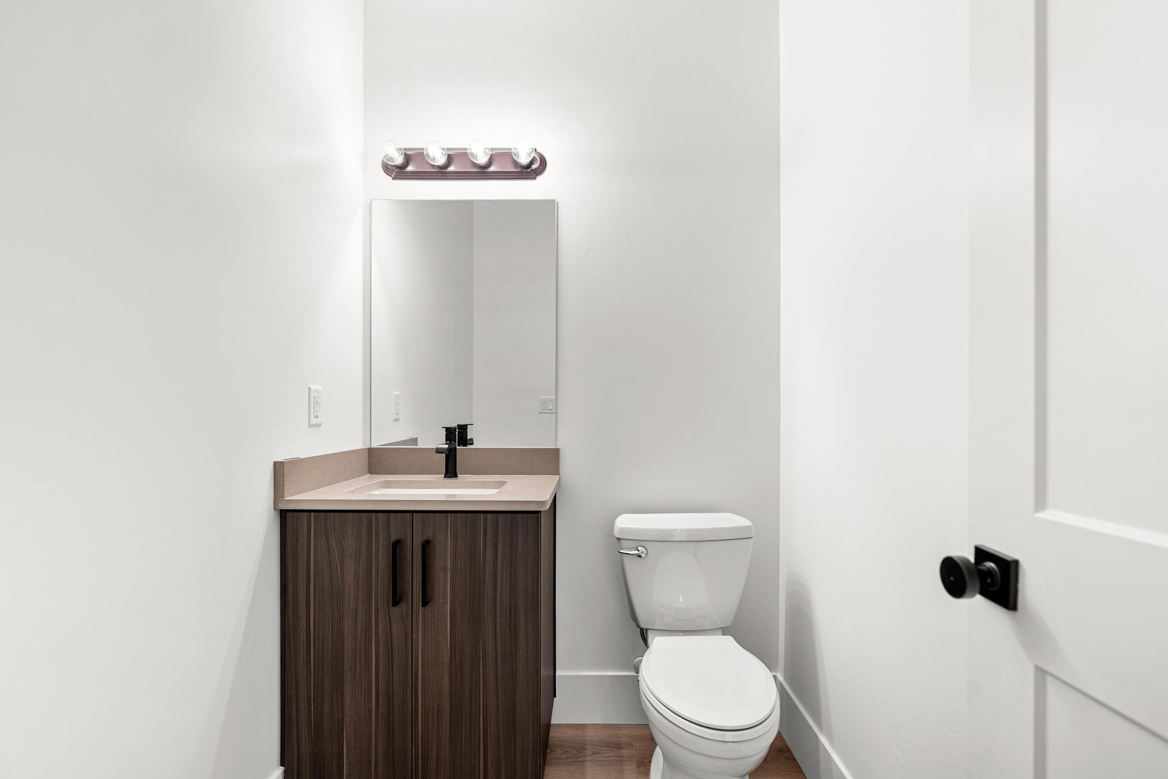 Contemporary powder room featuring a single vanity with wood-finish cabinetry, a light-toned countertop, and a rectangular undermount sink with a matte black faucet