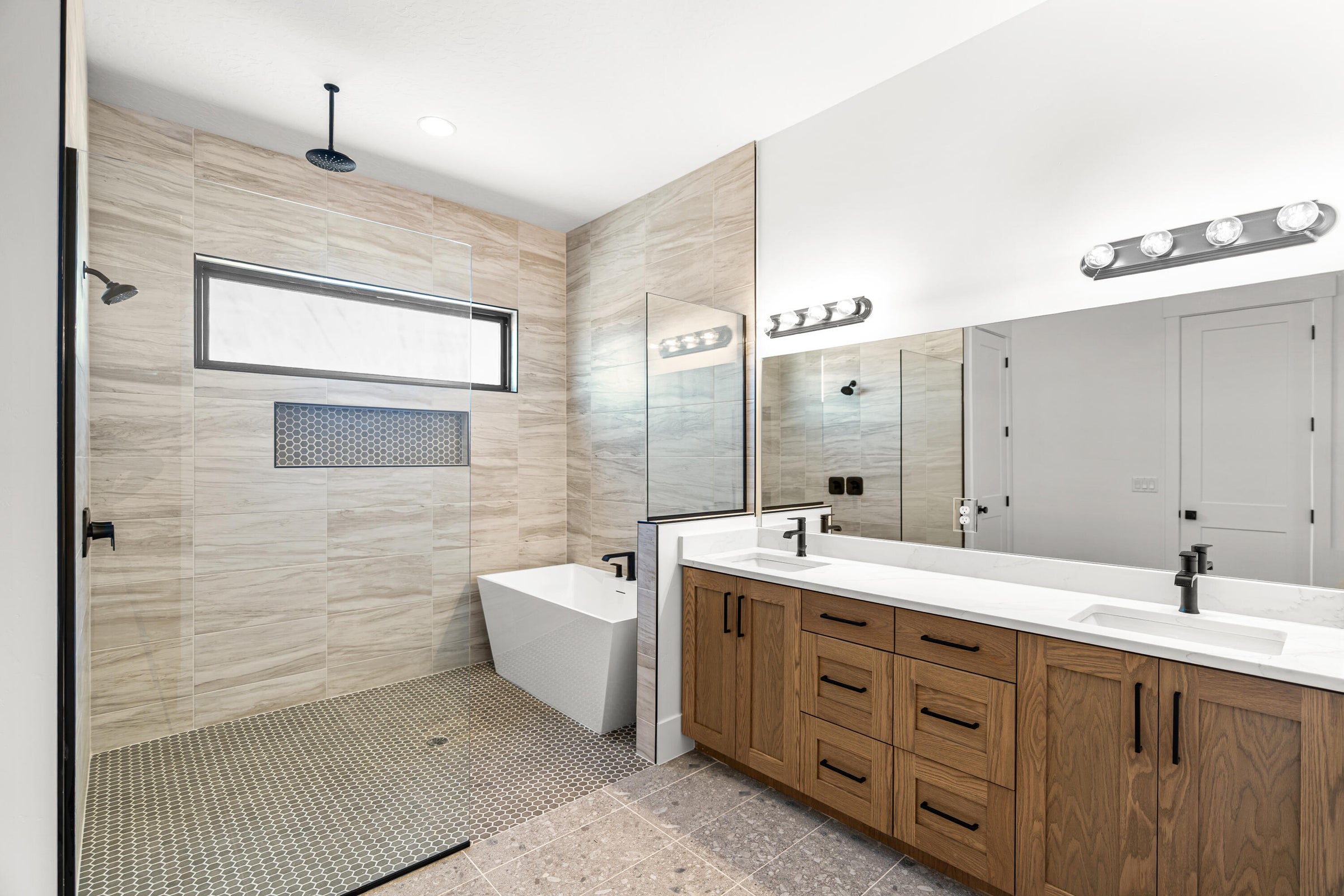 Spacious bathroom featuring a dual vanity with white countertops, a freestanding soaking tub, and a large walk-in shower with a rain showerhead