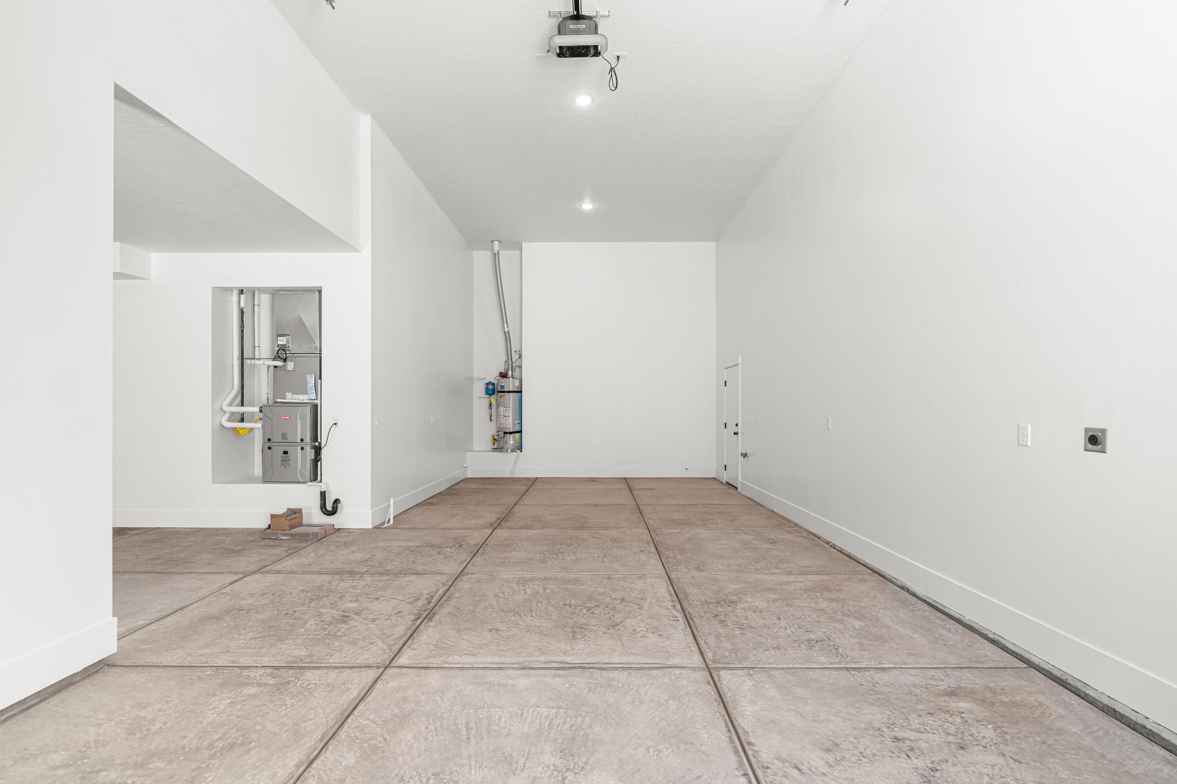 Spacious garage featuring a concrete floor with expansion joints, white painted walls, and an exposed utility alcove