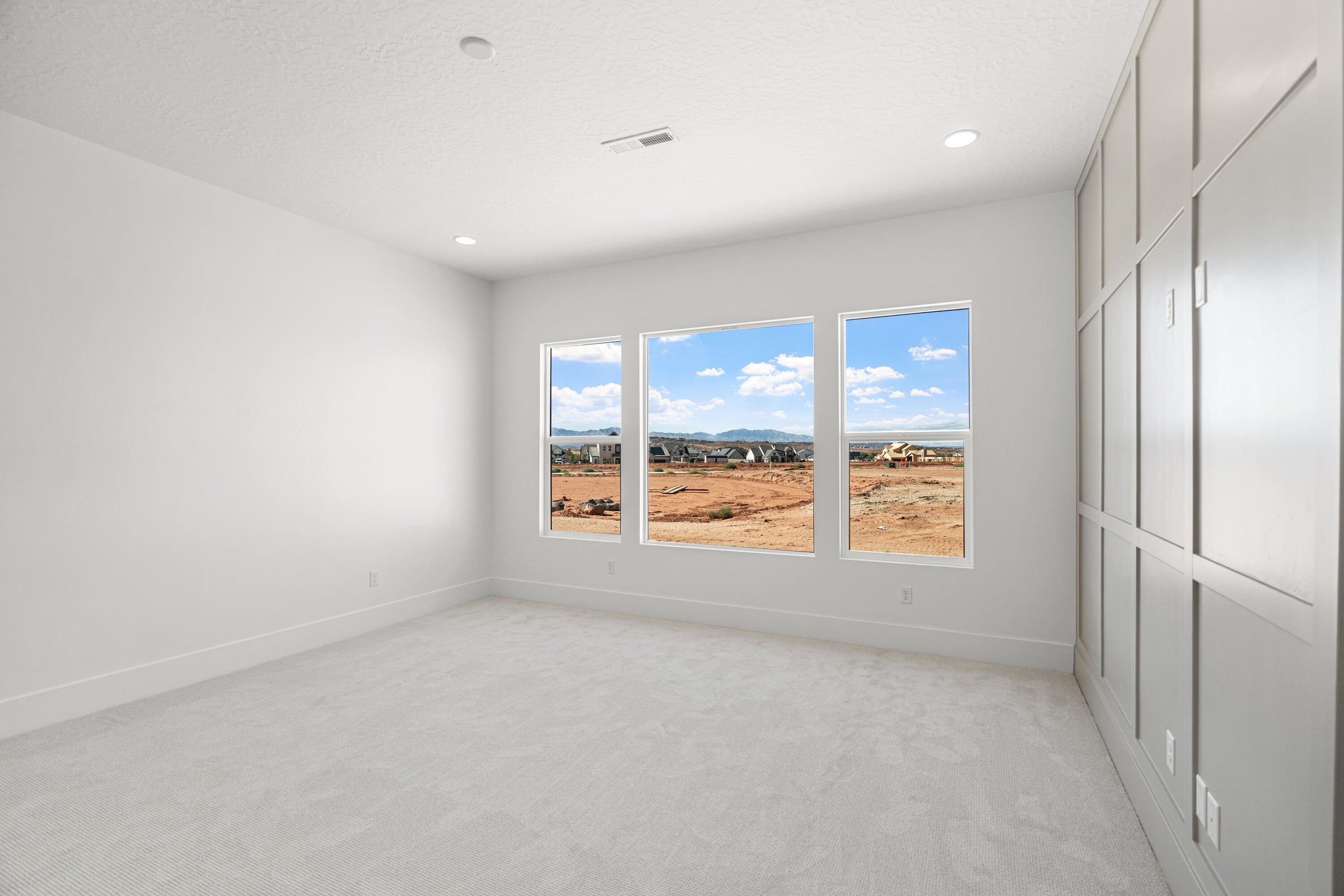 Spacious room featuring three large windows, white carpeting, recessed lighting, and a decorative board-and-batten accent wall