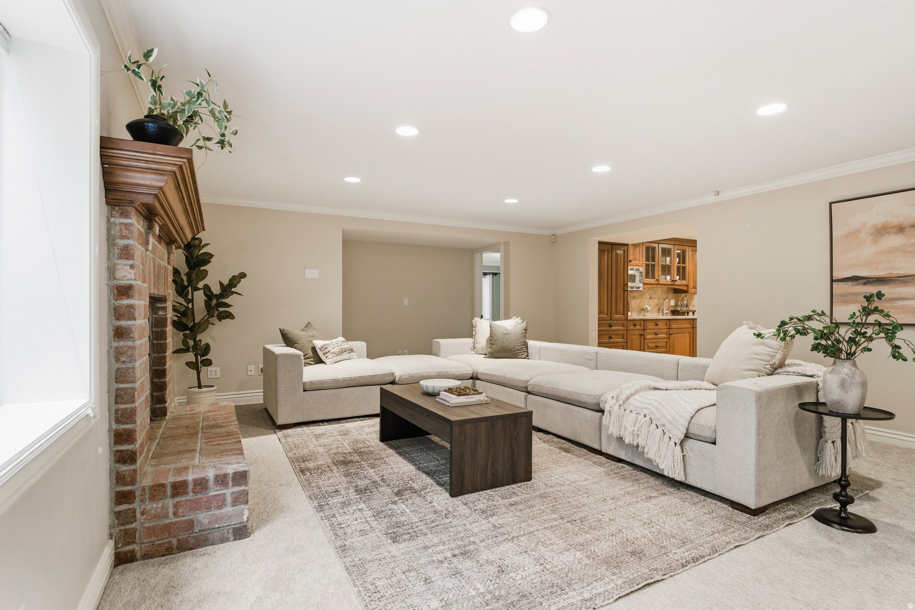 Spacious living area featuring a brick fireplace with a wood mantle, recessed lighting, crown molding, and neutral wall tones