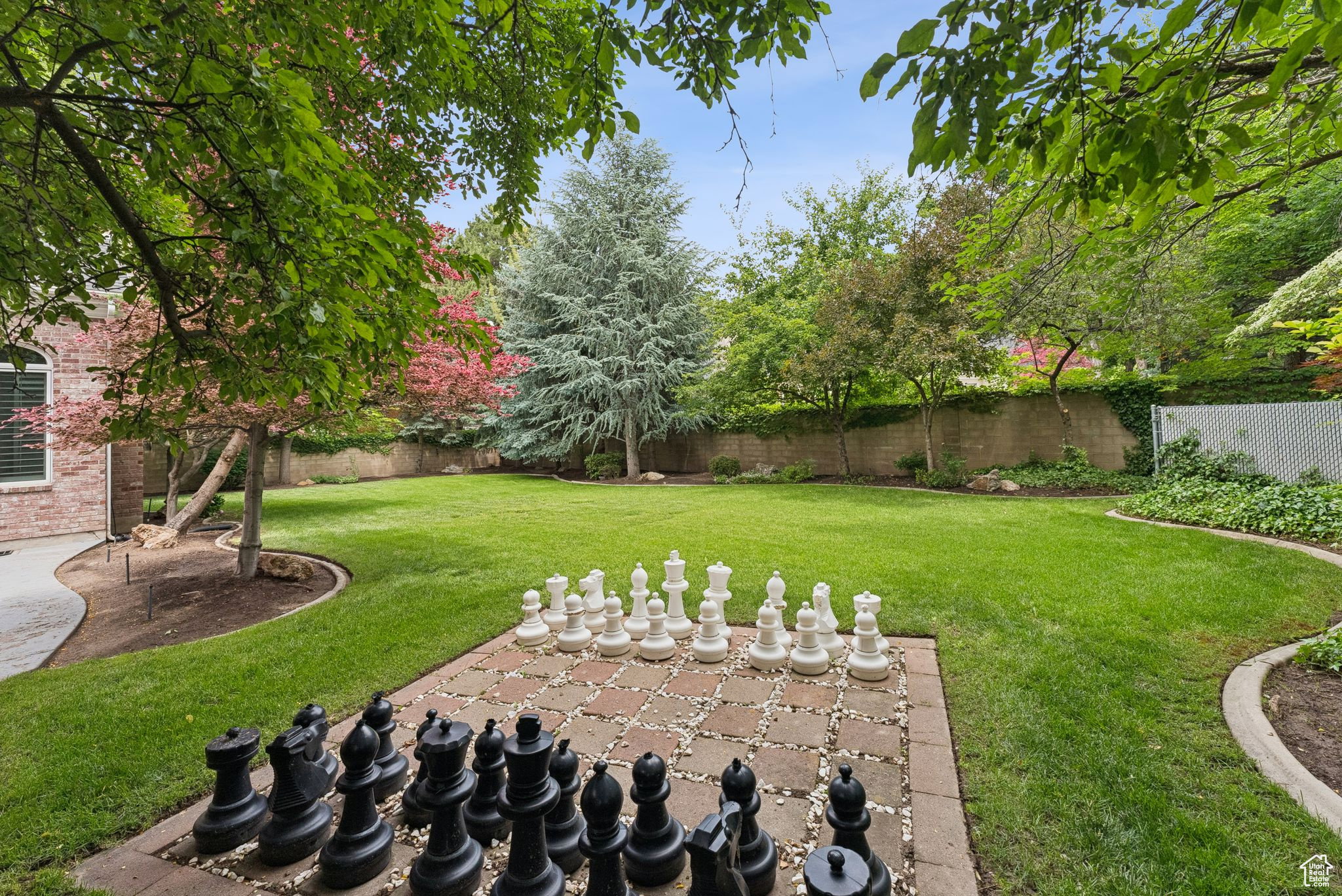 Expansive lawn area featuring a large-scale outdoor chess set on a paver patio