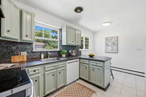 Kitchen featuring light green cabinetry, dark countertops, and a mosaic tile backsplash