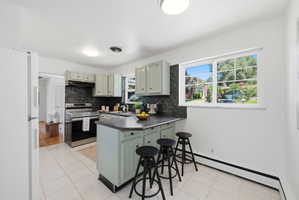 Kitchen featuring light-colored cabinetry with dark hardware, dark stone-finish countertops, and a full-height dark backsplash