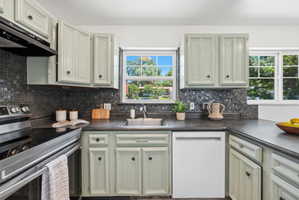 Kitchen featuring light-toned cabinetry with dark hardware, dark stone-look countertops, and a full-height mosaic tile backsplash