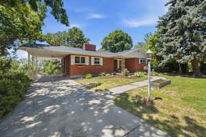 Brick exterior residence featuring a covered carport, established landscaping, and a concrete pathway leading to the front entry