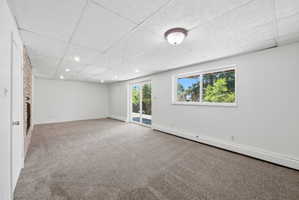Spacious room featuring neutral carpeting, a drop ceiling with recessed lighting, and a stone-front fireplace