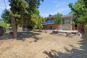 Expansive backyard featuring mature trees, a concrete patio, a concrete retaining wall, and a wood fence