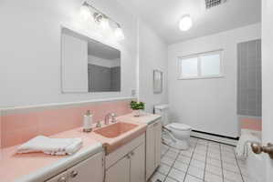 Bathroom featuring a tiled shower, white vanity with integrated pink sink, white toilet, and window