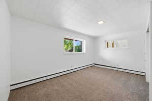 Carpeted interior room with white walls, a white acoustic tile ceiling, and two windows providing natural light