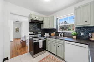 Kitchen with light green cabinetry, a mosaic tile backsplash, black countertops, and a stainless steel oven