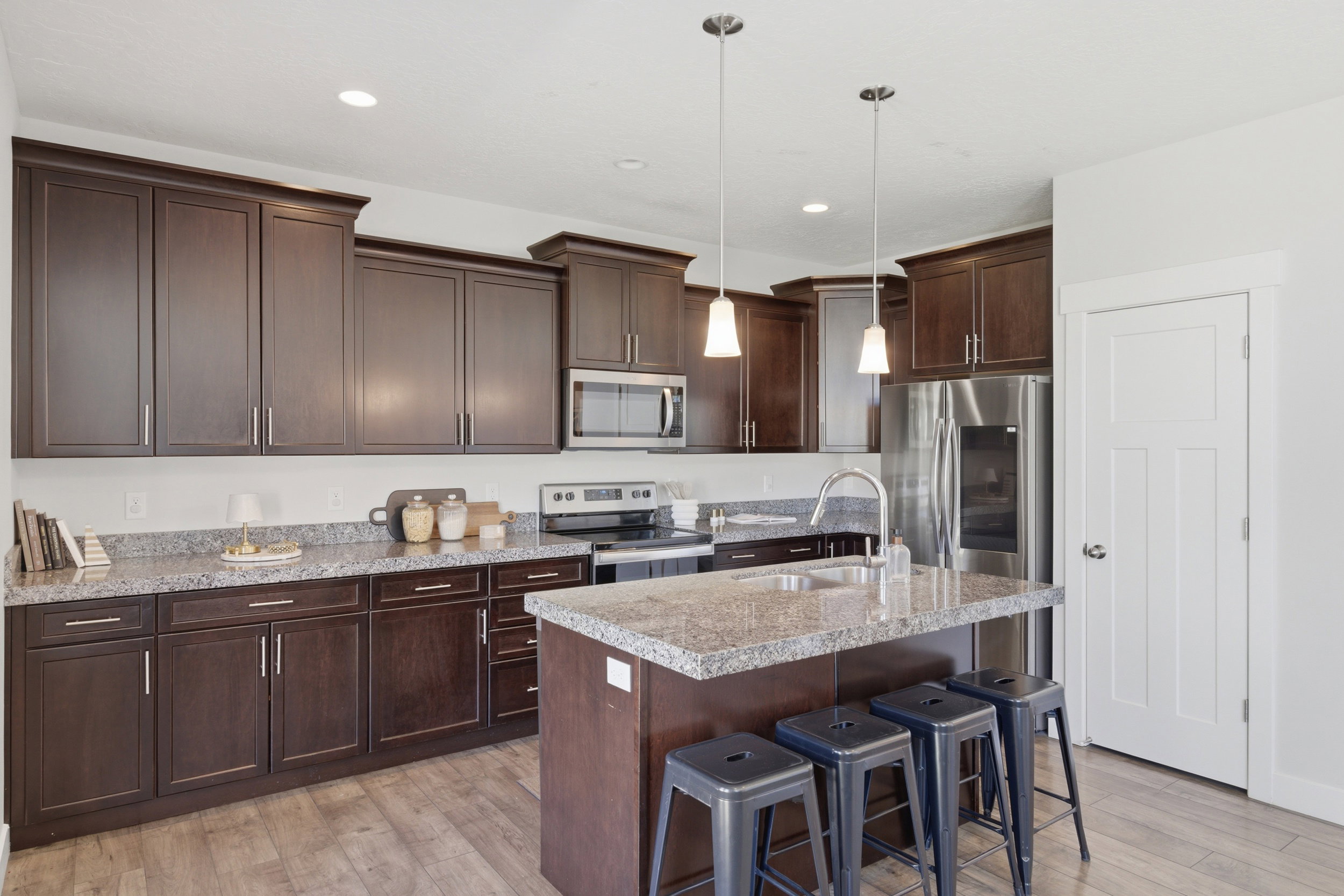 Kitchen featuring dark wood cabinetry, light-toned countertops, and a central island with a sink and pendant lighting