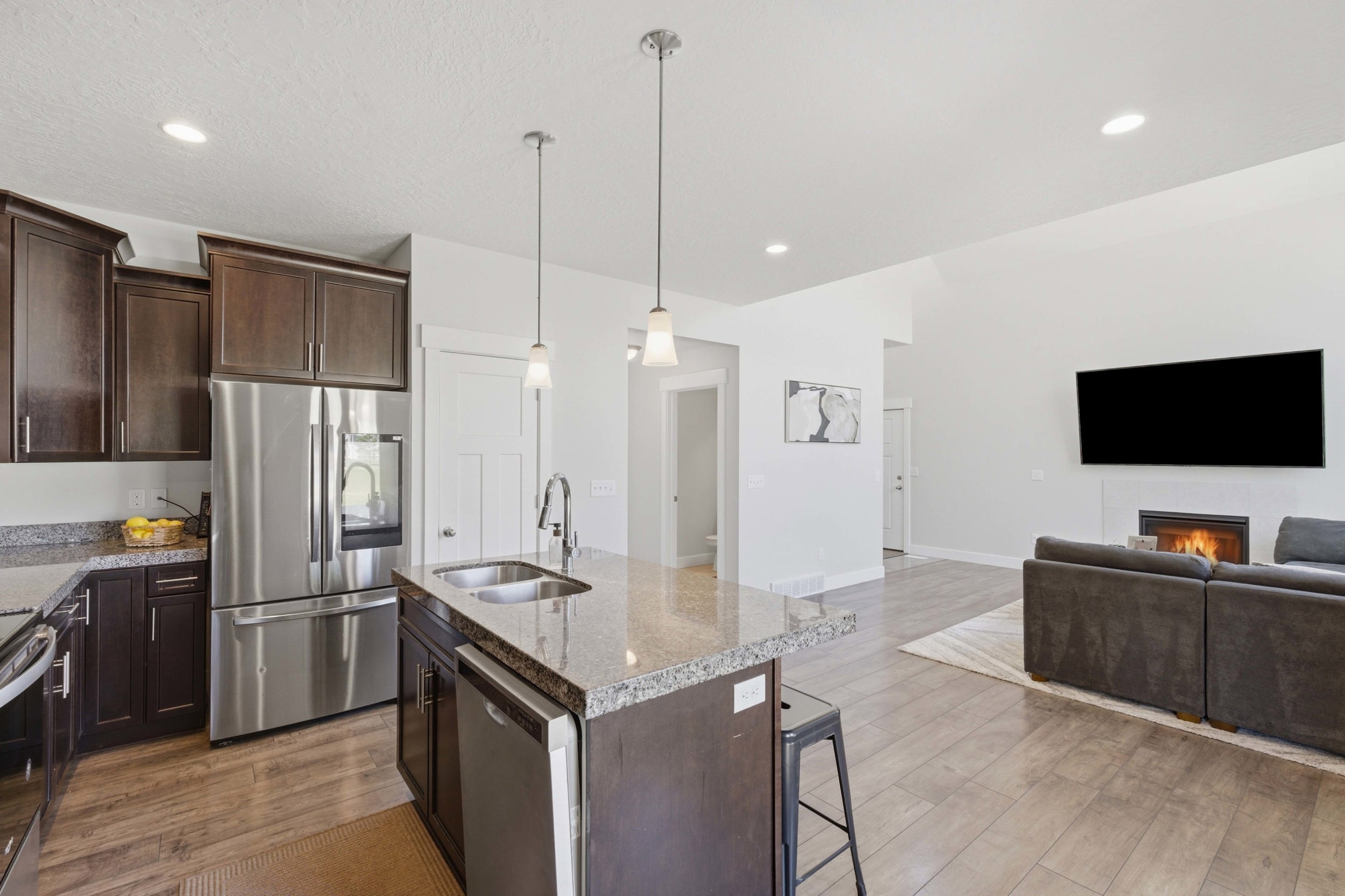 Open-concept living space featuring a kitchen island with dual basin sink and pendant lighting, dark wood-finish cabinetry, stainless steel appliances, and wood-finish flooring