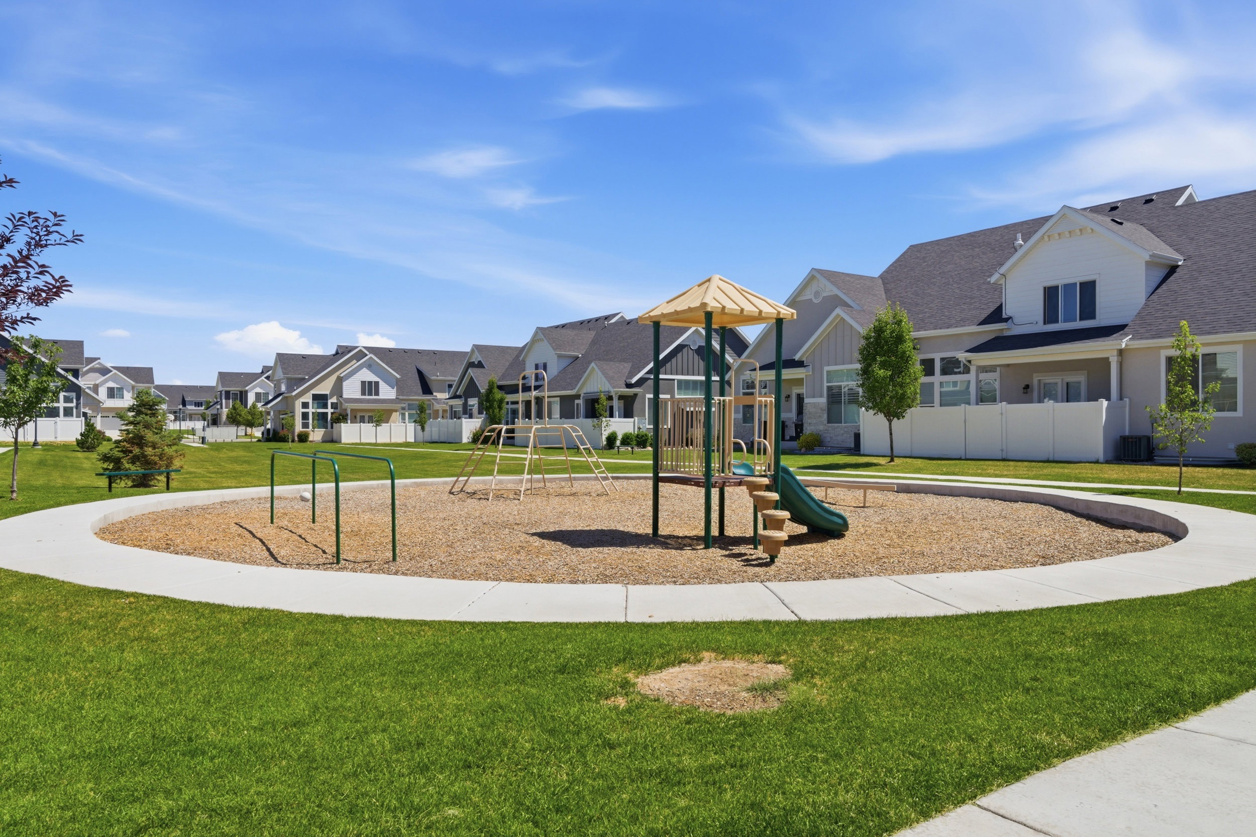Central playground featuring a slide, monkey bars, and a wood chip surface, encircled by a concrete path