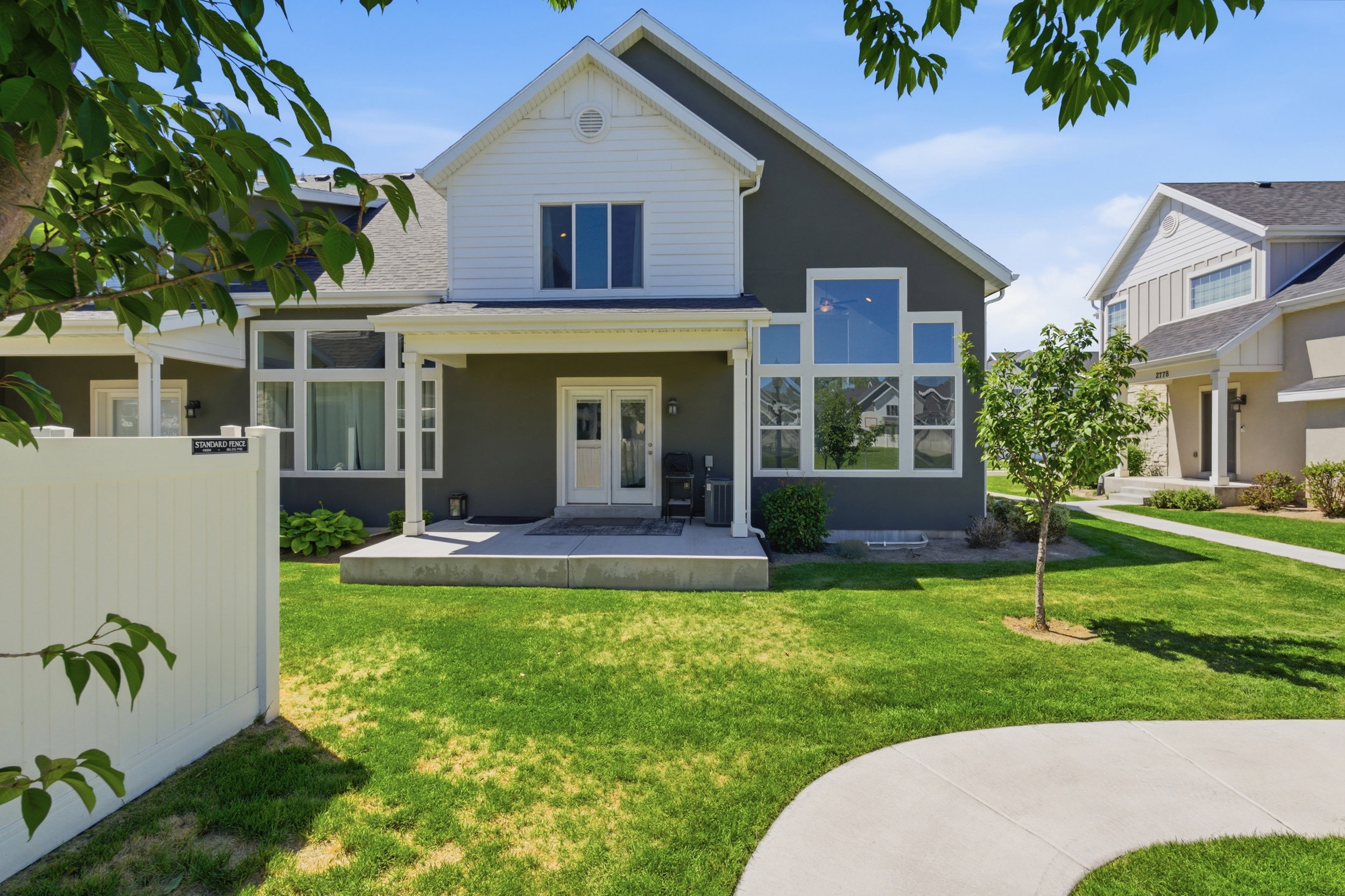 Rear exterior featuring a covered patio, double French doors, a large picture window, and a white privacy fence