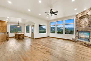 Spacious interior featuring wood-finish flooring, a stone fireplace with a hearth, and a series of large windows showcasing mountain scenery