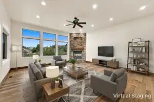 Spacious living area featuring large windows, wood-finish flooring, recessed lighting, and a stone-clad fireplace with a wood mantle