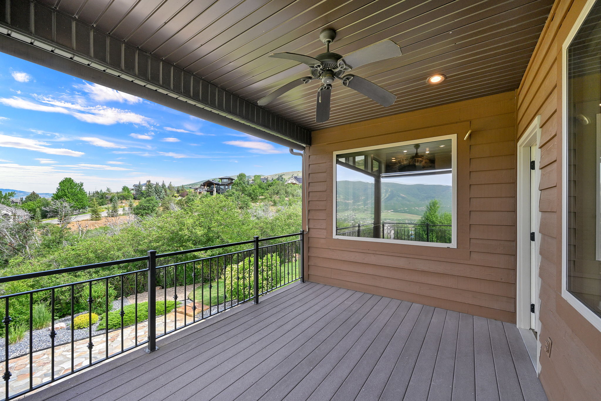 Expansive outdoor deck featuring wood-finish flooring, black metal railing, and a ceiling fan