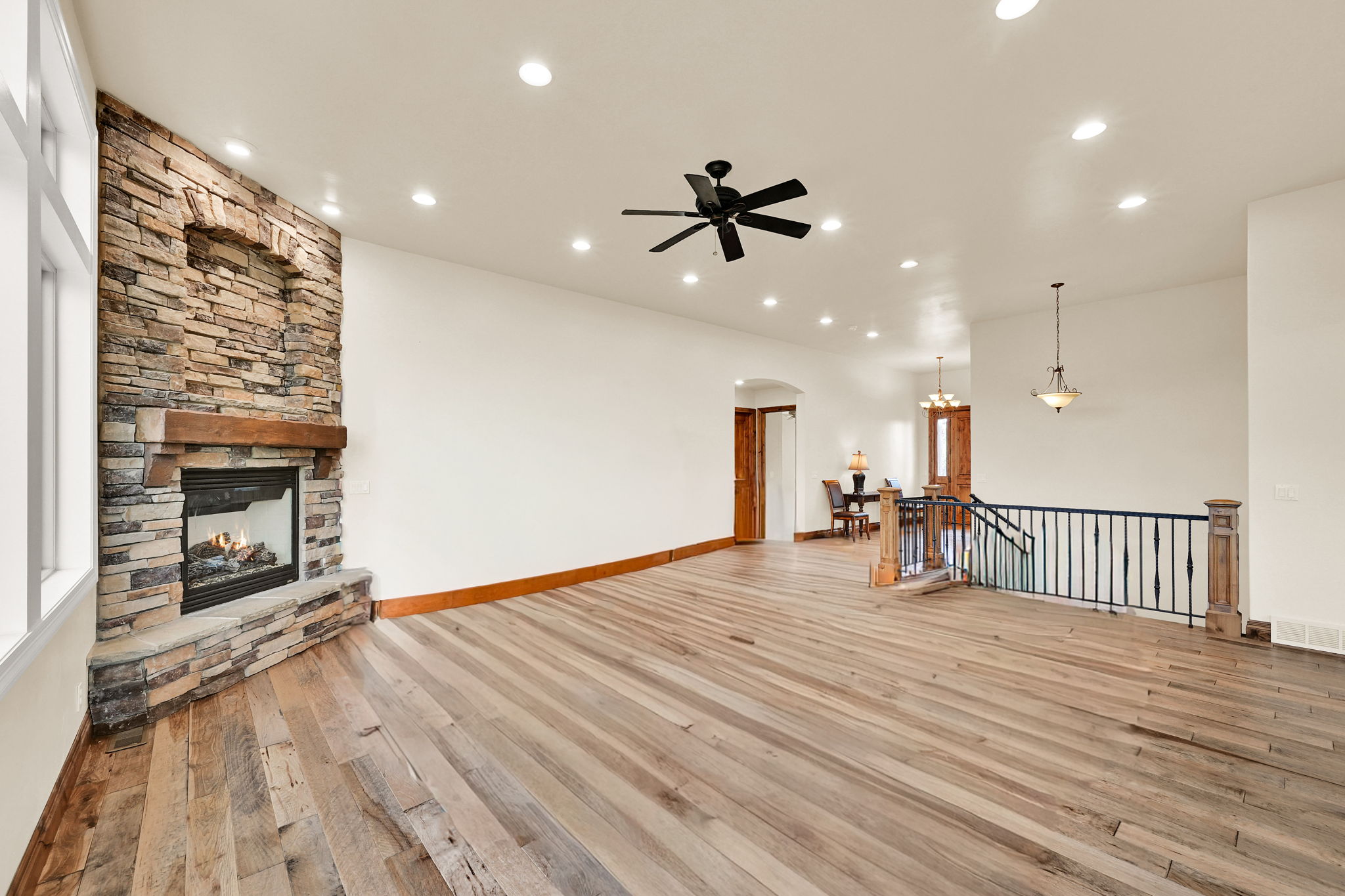 Spacious living area featuring a floor-to-ceiling stone fireplace with a wood mantel, wide plank wood-finish flooring, recessed lighting, and a ceiling fan