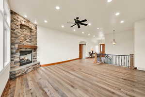 Spacious living area featuring a floor-to-ceiling stone fireplace with a wood mantel, wide plank wood-finish flooring, recessed lighting, and a ceiling fan