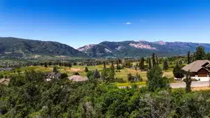 Expansive mountain landscape featuring a vibrant green valley, mature trees, and residential properties