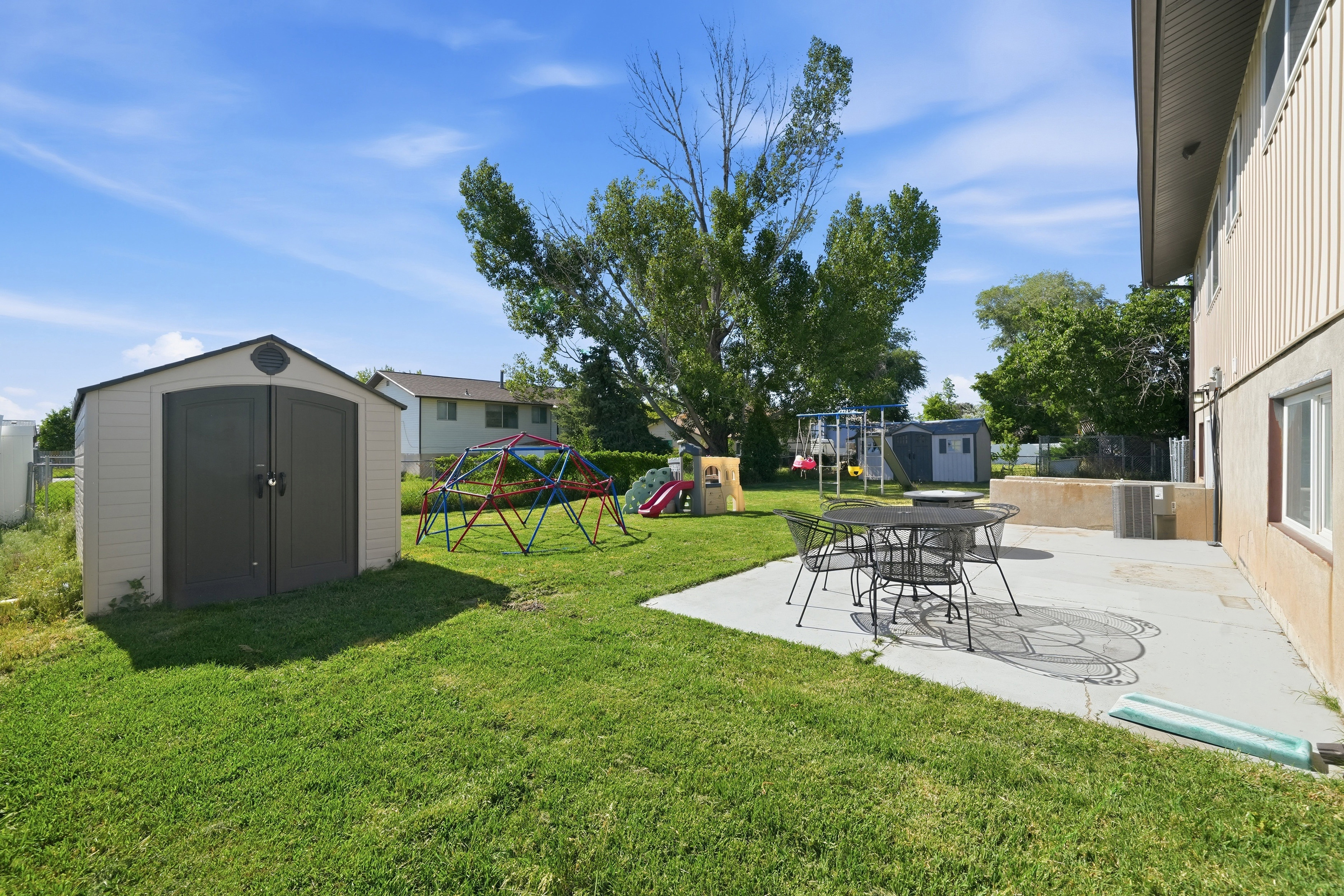 Expansive backyard featuring a concrete patio, mature trees, and a detached storage shed